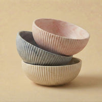 Three 'emilie bol halo' ceramic bowls of different colors stacked on a beige background